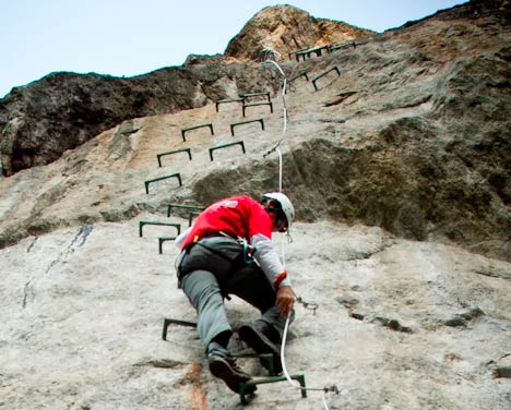 Persona ascendiendo la vía ferrata de Les por clavijas de acero