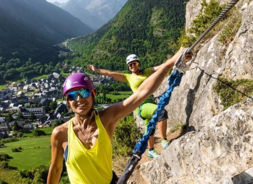 Dos personas en la via ferrata Eth Taro d'Arties, con el pueblo de Arties y el valle al fondo